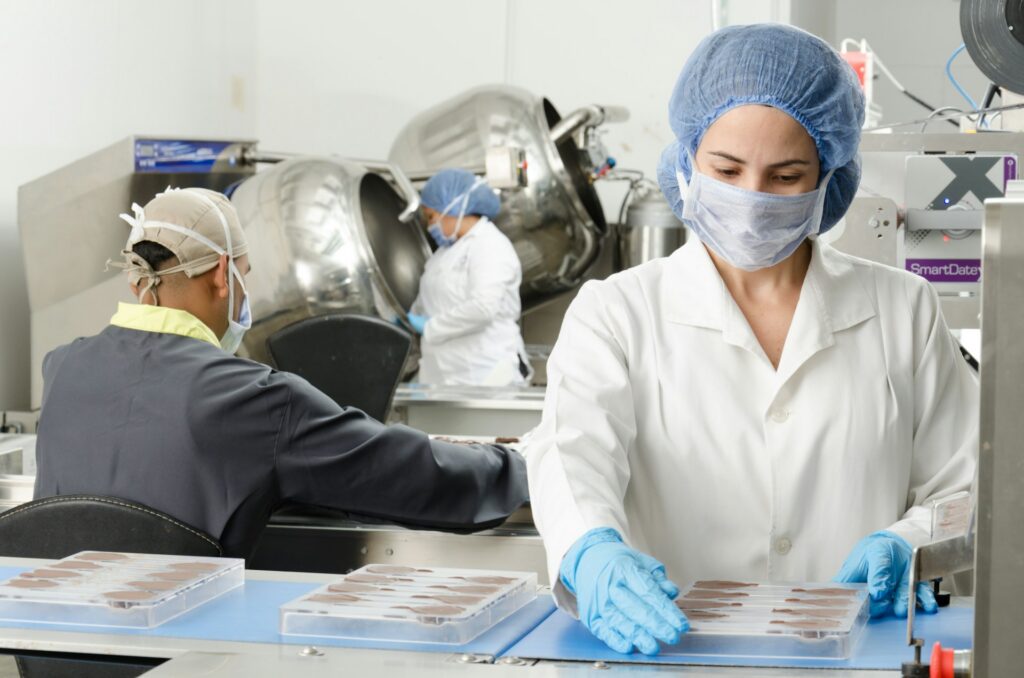 Operarios con mascarilla y bata trabajando en el interior de una planta de producción